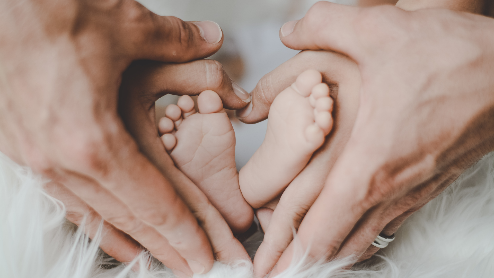 Babyfüsse in zwei Paar zu Herzen geformten Händen